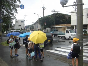 にわか雨が降り始め，傘をさし信号を待つ子どもたち(7:40)