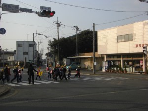 やわらかな朝の日差しを浴びながら，鹿島小前交差点を横断する子どもたち(7:55)